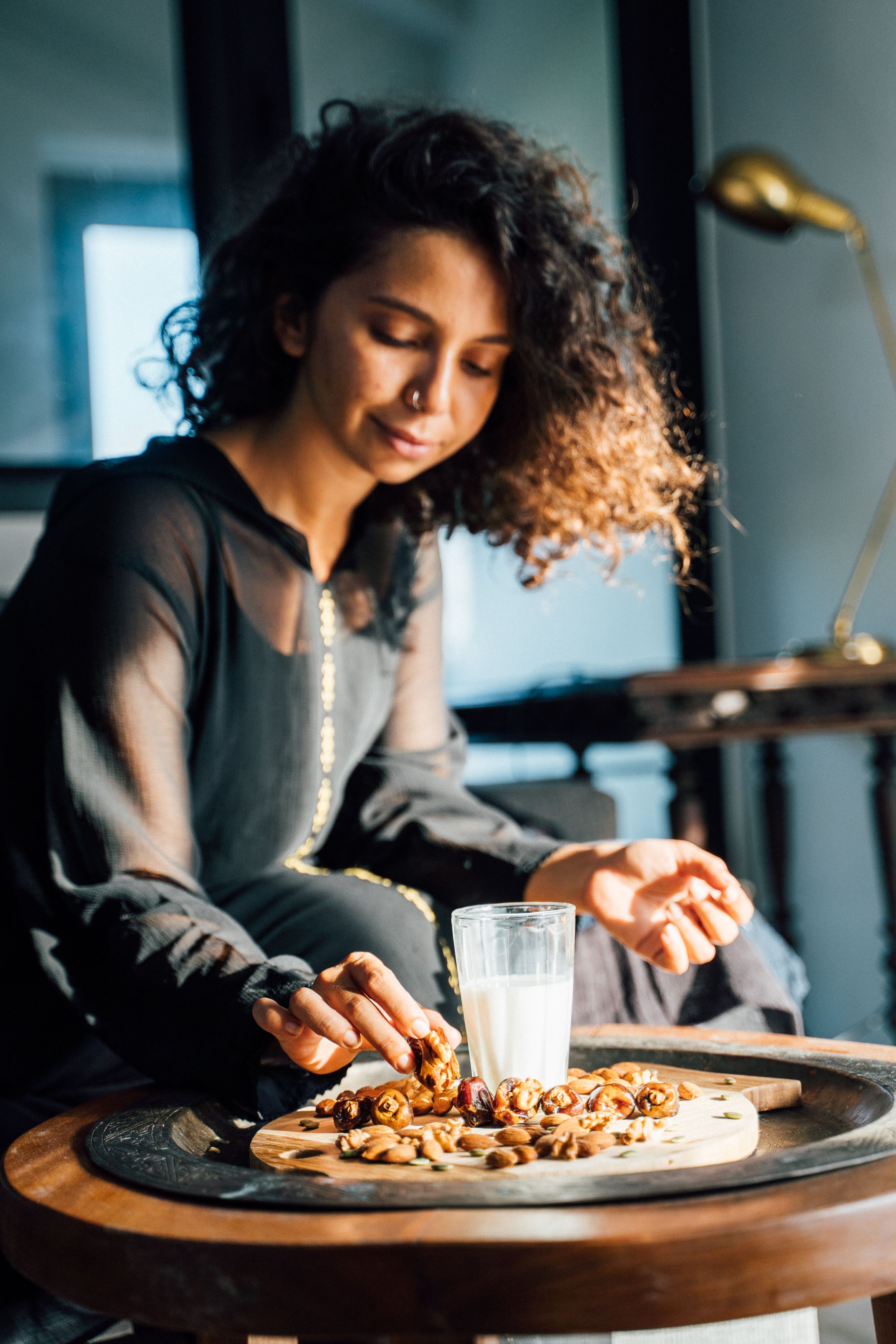 Woman picking dates and almonds from a wooden board next to a glass of milk