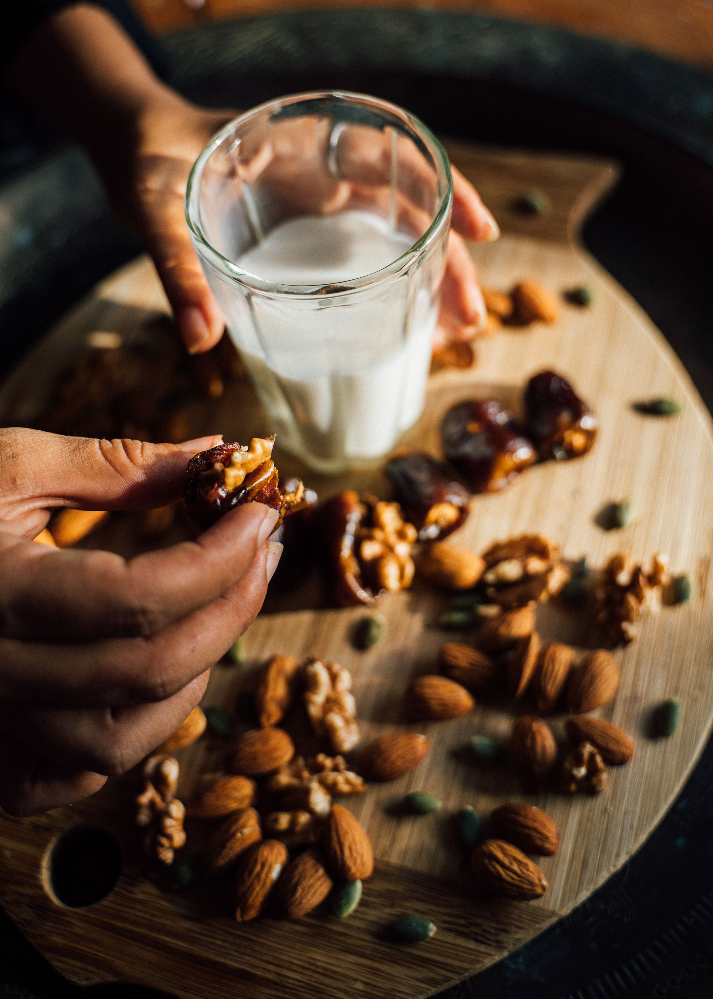 Hands holding a walnut-stuffed date over a board of almonds and walnuts